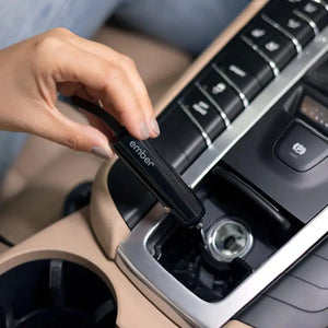 Käsi ühendamas Ember elektrilise tassi autolaadijat auto sigaretisüütaja pistikusse mugavaks laadimiseks.
